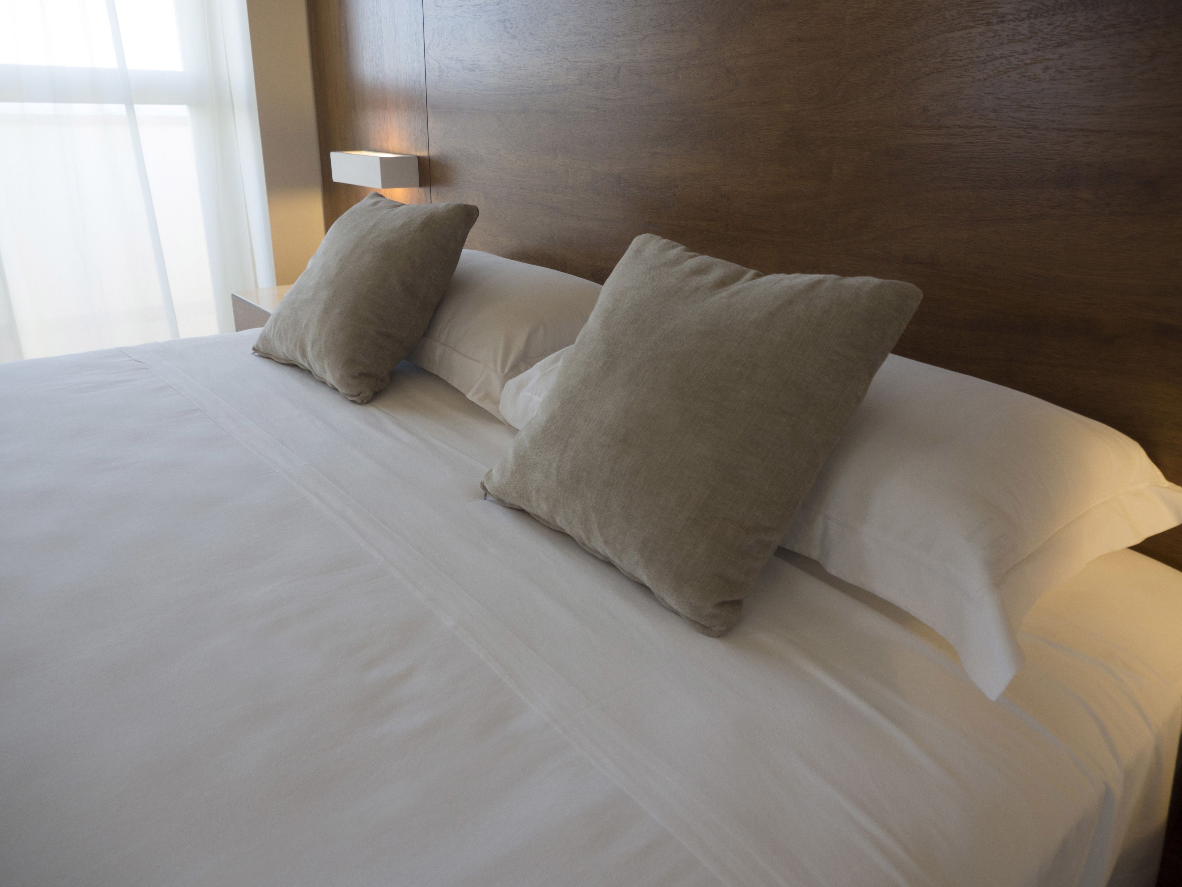 A neatly made bed with white linens and two beige pillows.