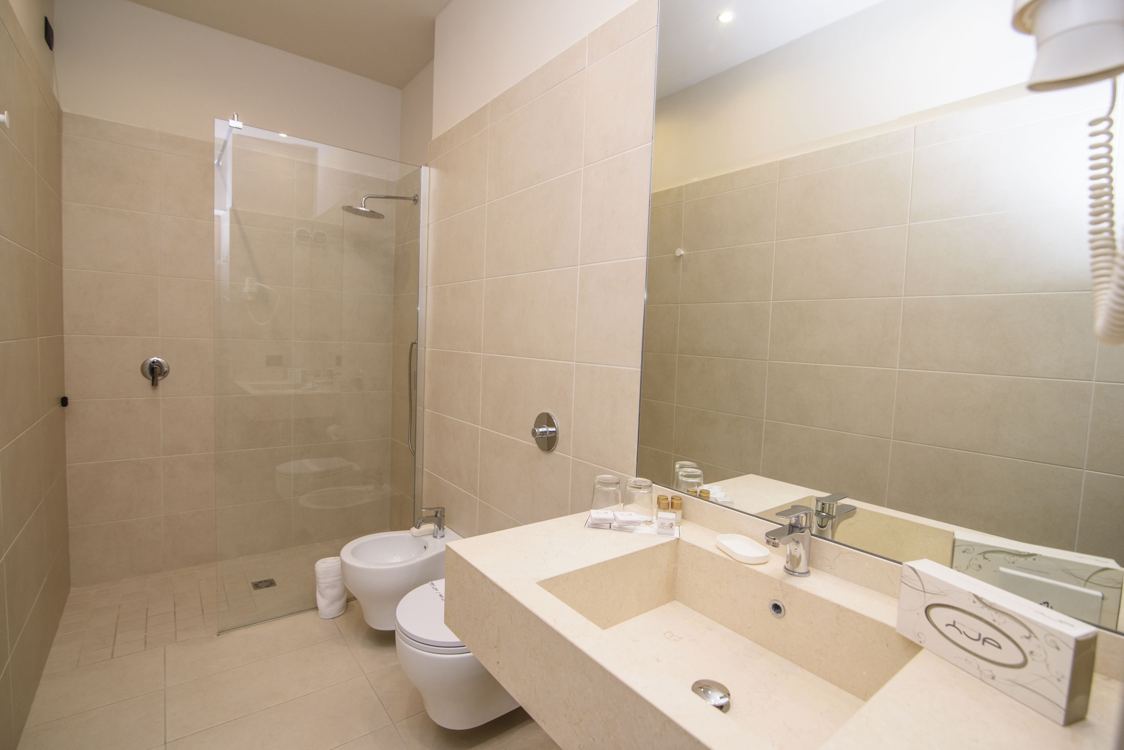 A modern bathroom with a glass shower enclosure, a bidet, a sink with a mirror, and a toilet.