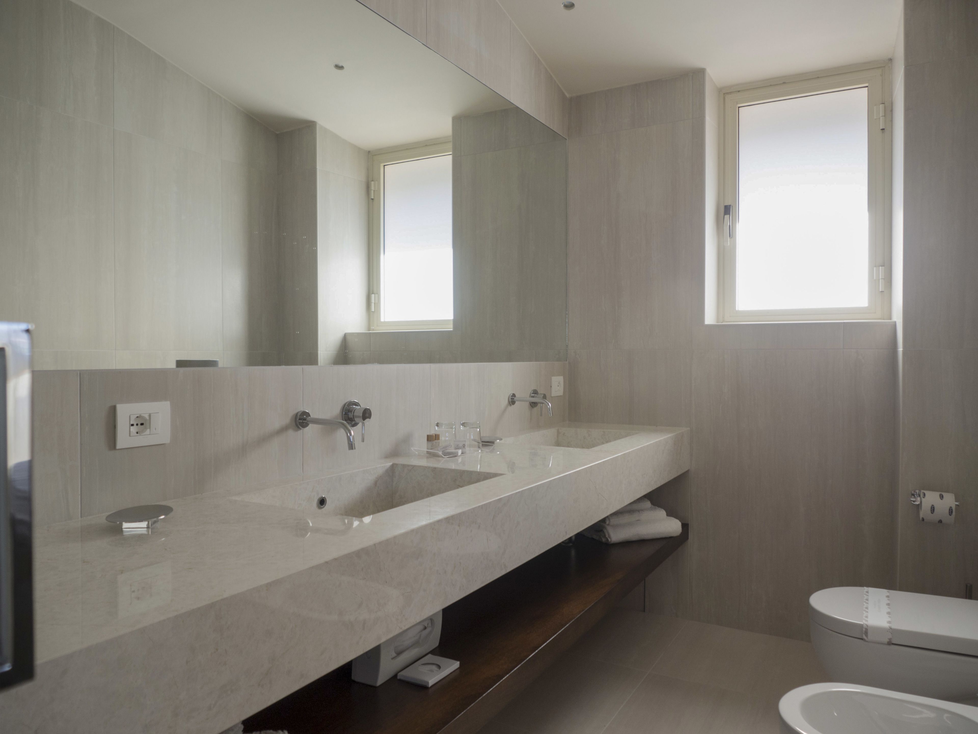 Un bagno moderno con uno specchio grande, due lavandini e un water.