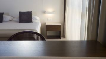 A hotel room with a bed, a bedside table, a chair, and a window with curtains.