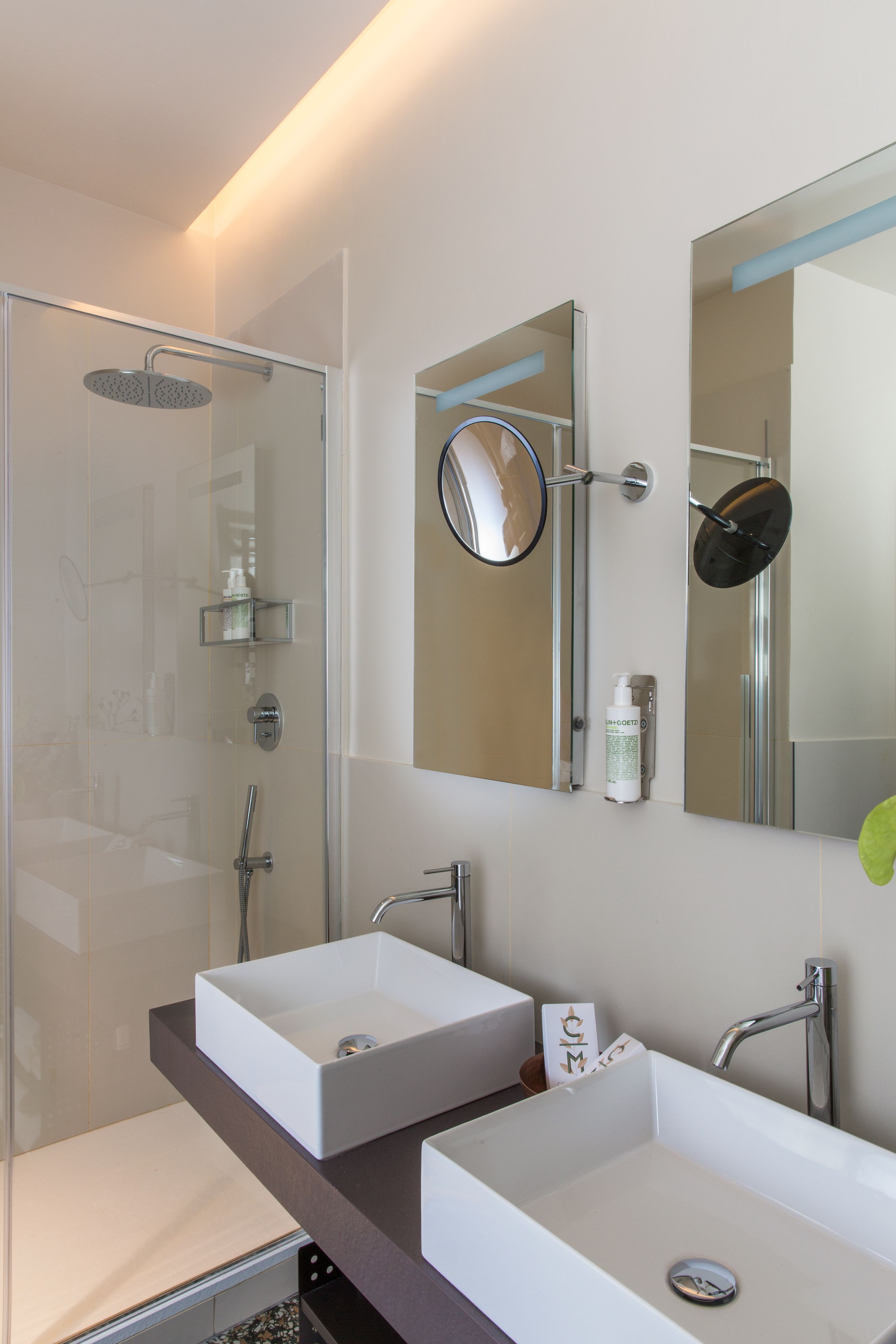 A modern bathroom with a glass-enclosed shower, two white sinks, and a large mirror.