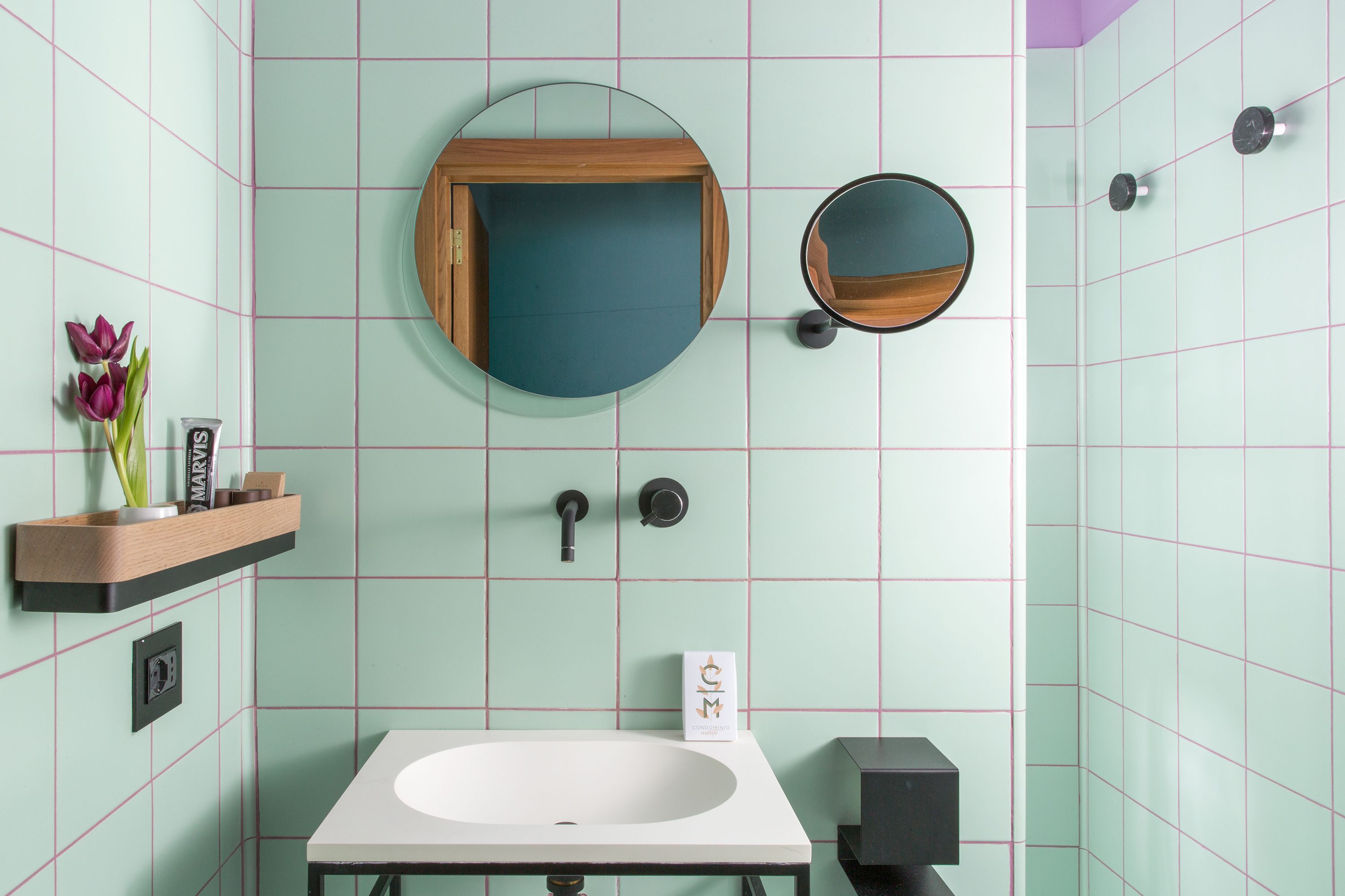 A bathroom with a white sink, a wooden shelf with toiletries, a mirror, and a clock on the wall.