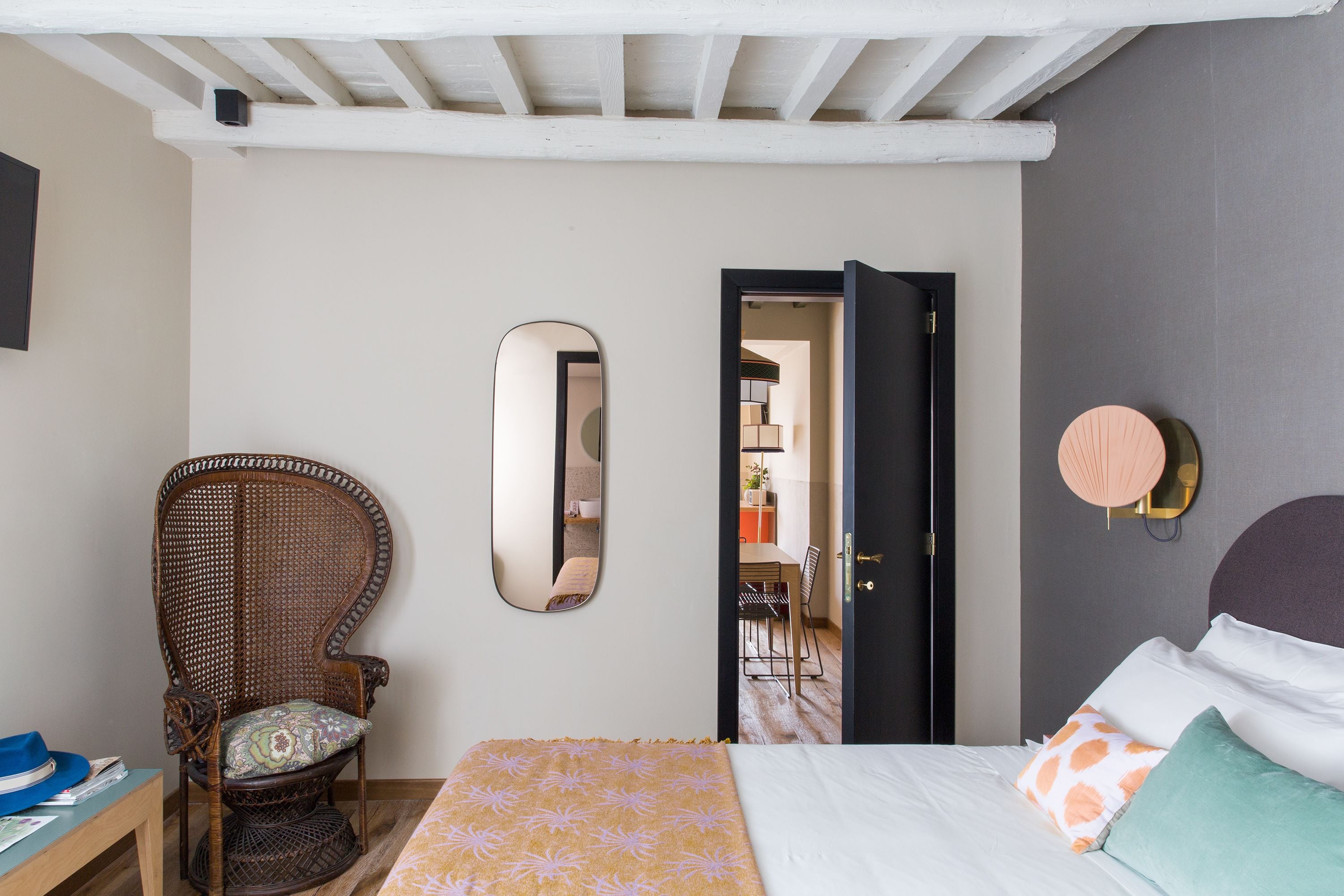 Een slaapkamer met een bed, een stoel, een spiegel en een deur naar een andere kamer.