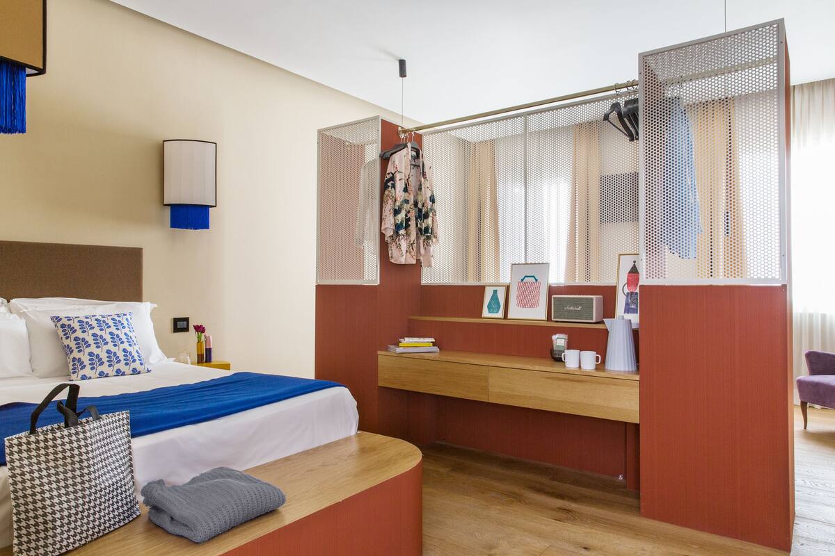 A hotel room with a bed, a desk, a chair, a wardrobe, and a bathroom area.