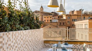 An outdoor dining area with checkered tile walls, tables with metal chairs, and a view of historic buildings in the background. - Condominio Monti Boutique Hotel (Rome)