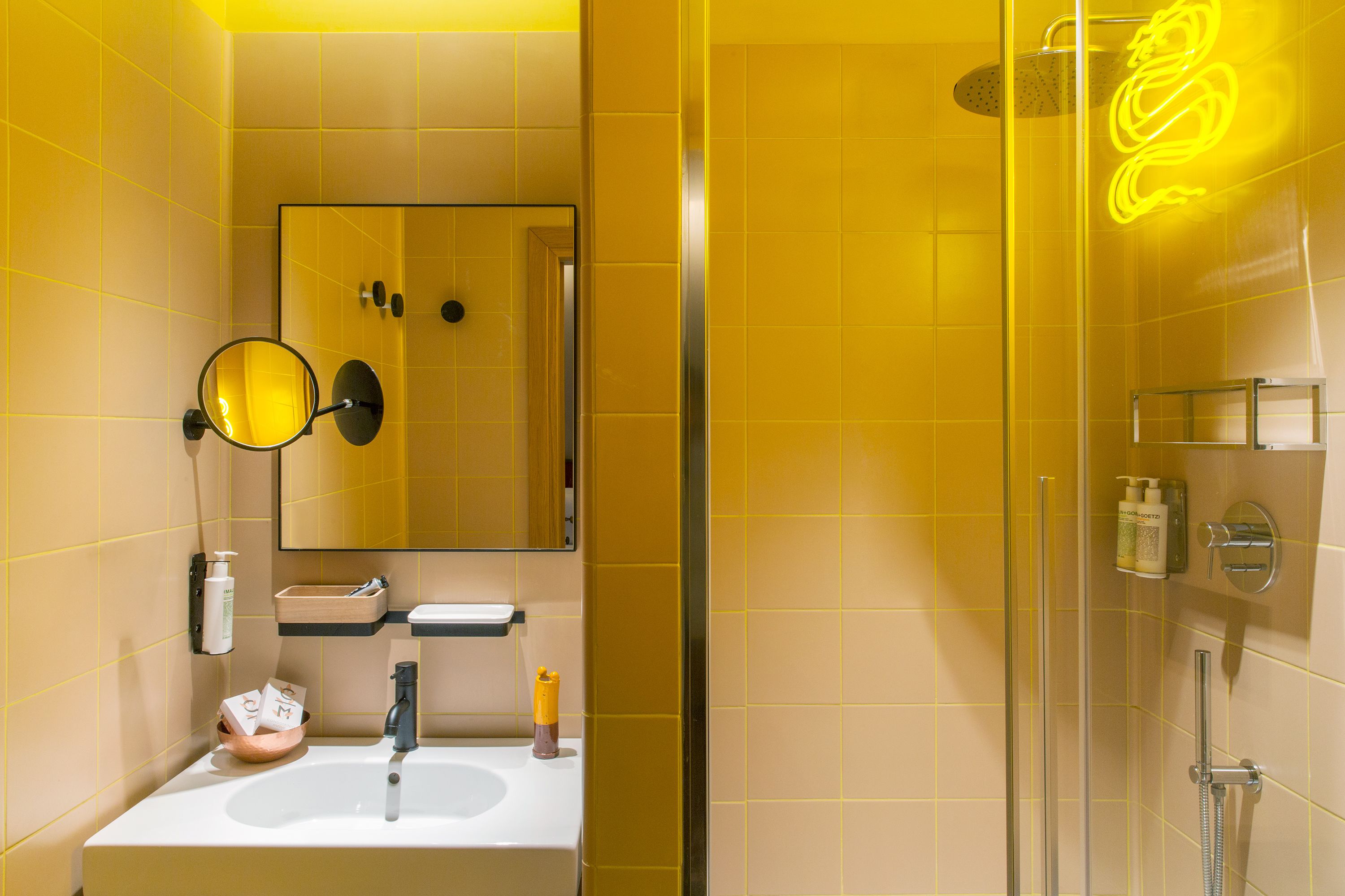 A modern bathroom with a glass shower enclosure, a white sink, and a mirror with a round frame.
