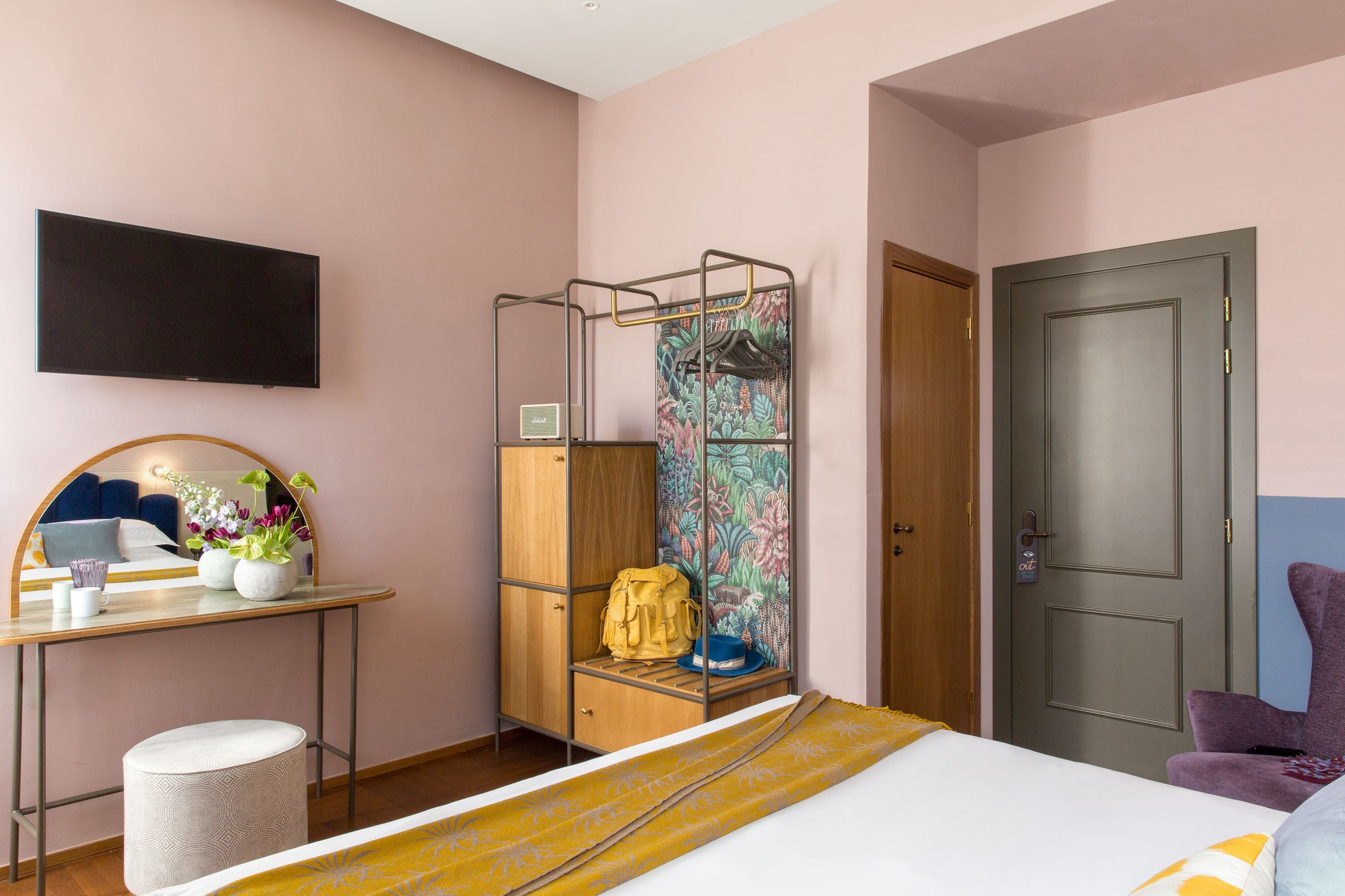 A bedroom with a bed, a desk with a mirror, a TV, a wardrobe, and a door.
