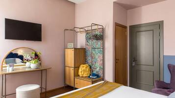 A bedroom with a bed, a desk with a mirror, a TV, a wardrobe, and a door.