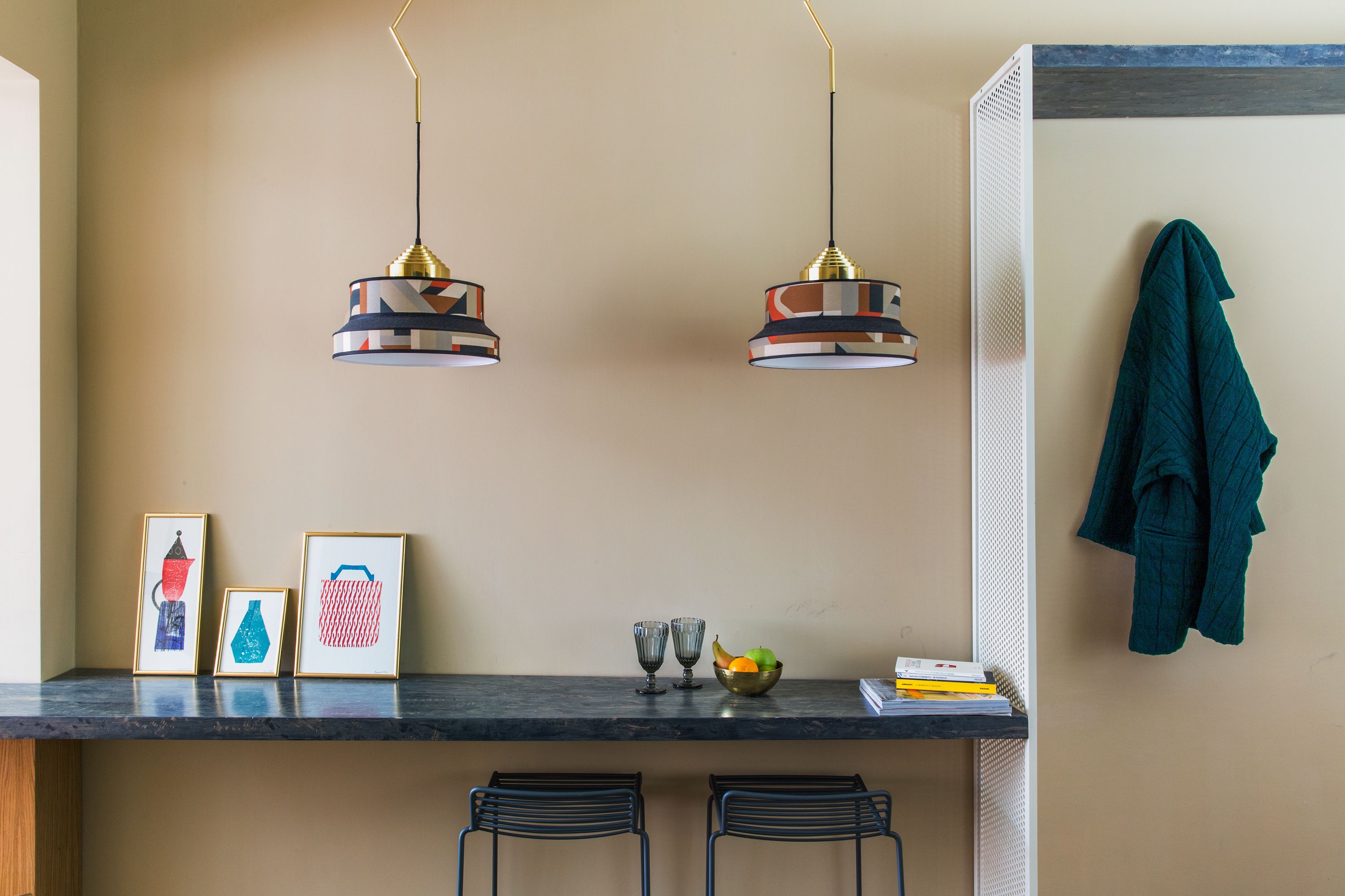 A kitchen with two hanging pendant lights, a countertop with framed artwork, a fruit bowl, and a towel hanging on a rack.
