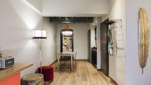 A hallway with a wooden floor, a red ottoman, a table with chairs, a lamp, and a wall-mounted decorative leaf. - Condominio Monti Boutique Hotel (Rome)