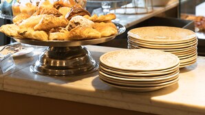 A buffet with pastries and fruits, a stack of plates, and a view of buildings through a window. - Condominio Monti Boutique Hotel (Rome)