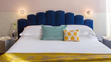 A neatly made bed with a blue headboard, a green and a yellow patterned pillow, and a yellow bedspread.