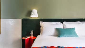 A hotel room with a bed, a nightstand, a lamp, and a red side table.