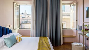 A hotel room with a bed, a window with curtains, a small table with a vase, and a view of buildings outside. - Condominio Monti Boutique Hotel (Rome)
