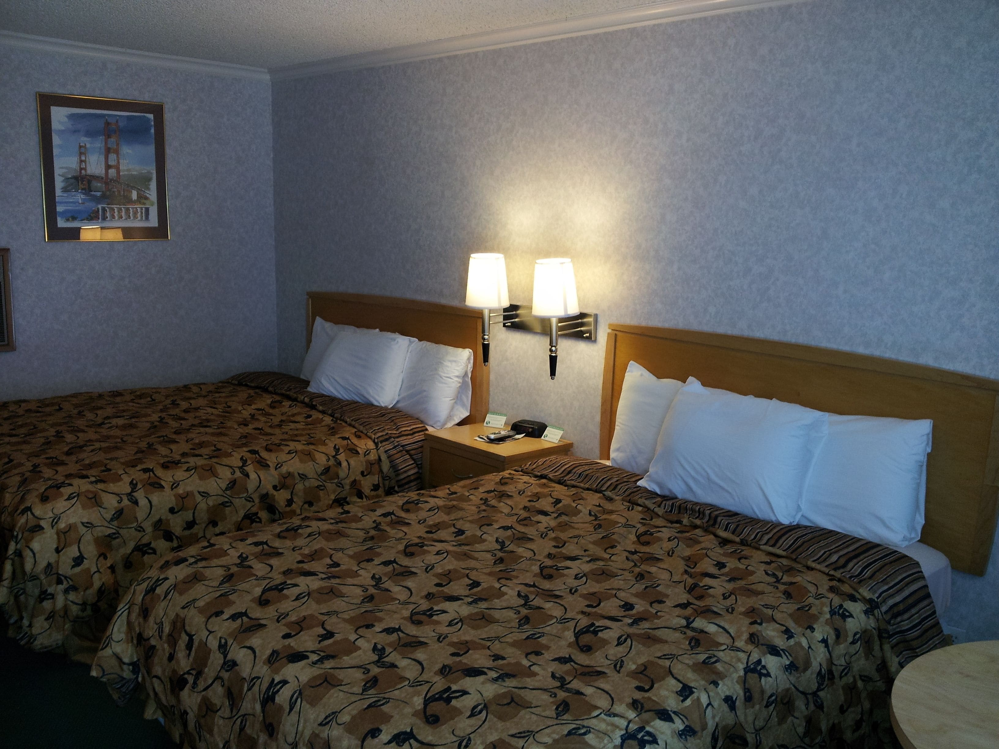 A hotel room with two beds, each with a floral-patterned bedspread, a wooden headboard, and a nightstand with a lamp.
