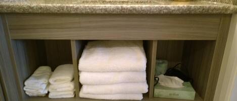 Un baño con encimera, lavamanos y estante con toallas dobladas y una caja de pañuelos.