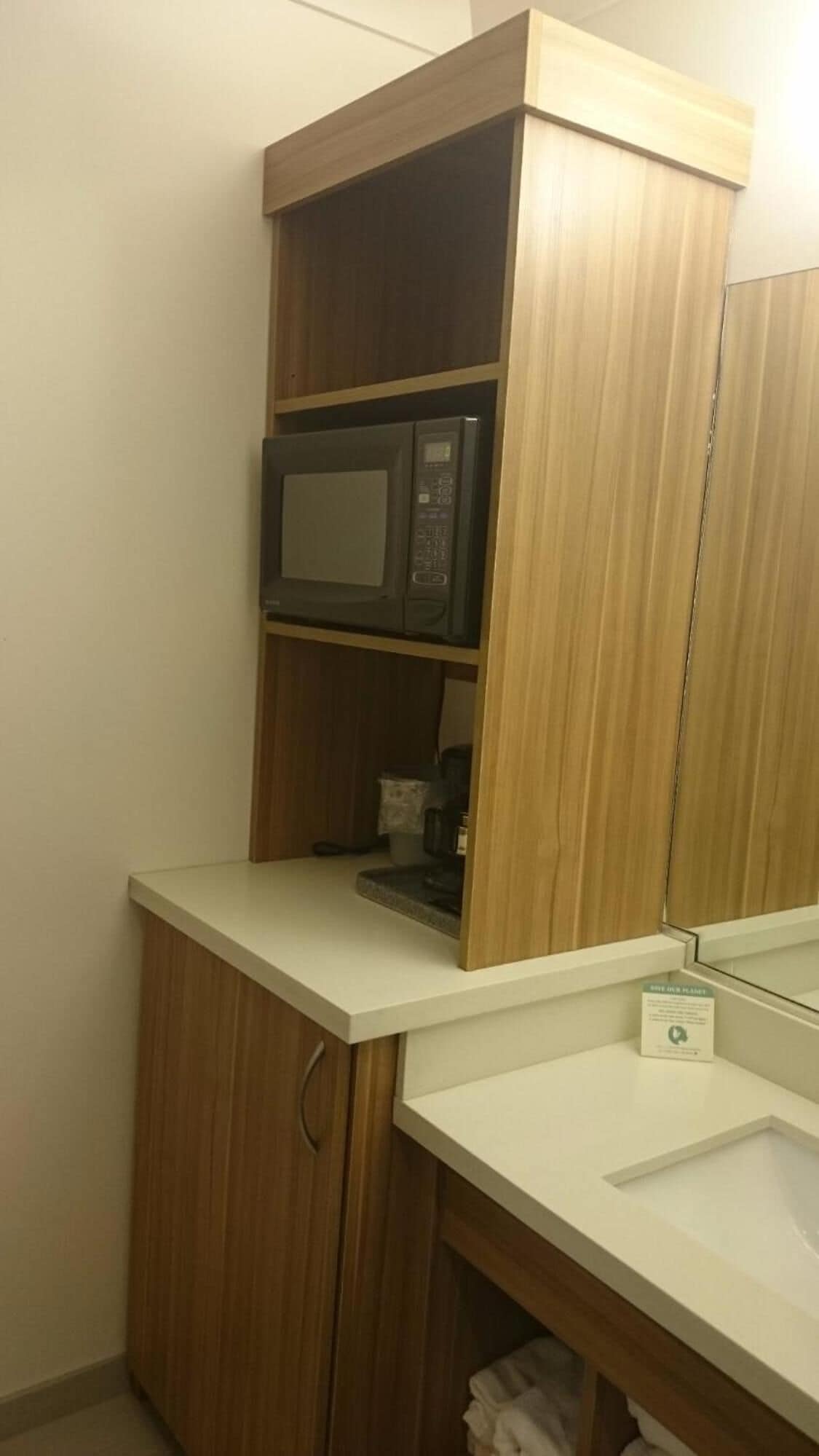 Un baño con un mueble de madera, un microondas y un lavamanos.