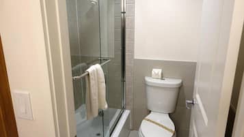 A bathroom with a glass-enclosed shower, a toilet with a decorative strip, and a towel rack with two towels.