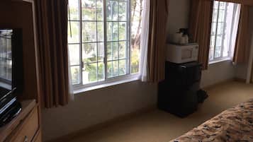 A hotel room with a large window, a bed with a floral bedspread, a dresser, a microwave, and a television.