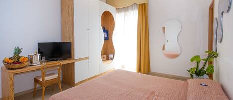 Una habitación de hotel con una cama, un escritorio con televisor, un armario de madera, un espejo y una planta.