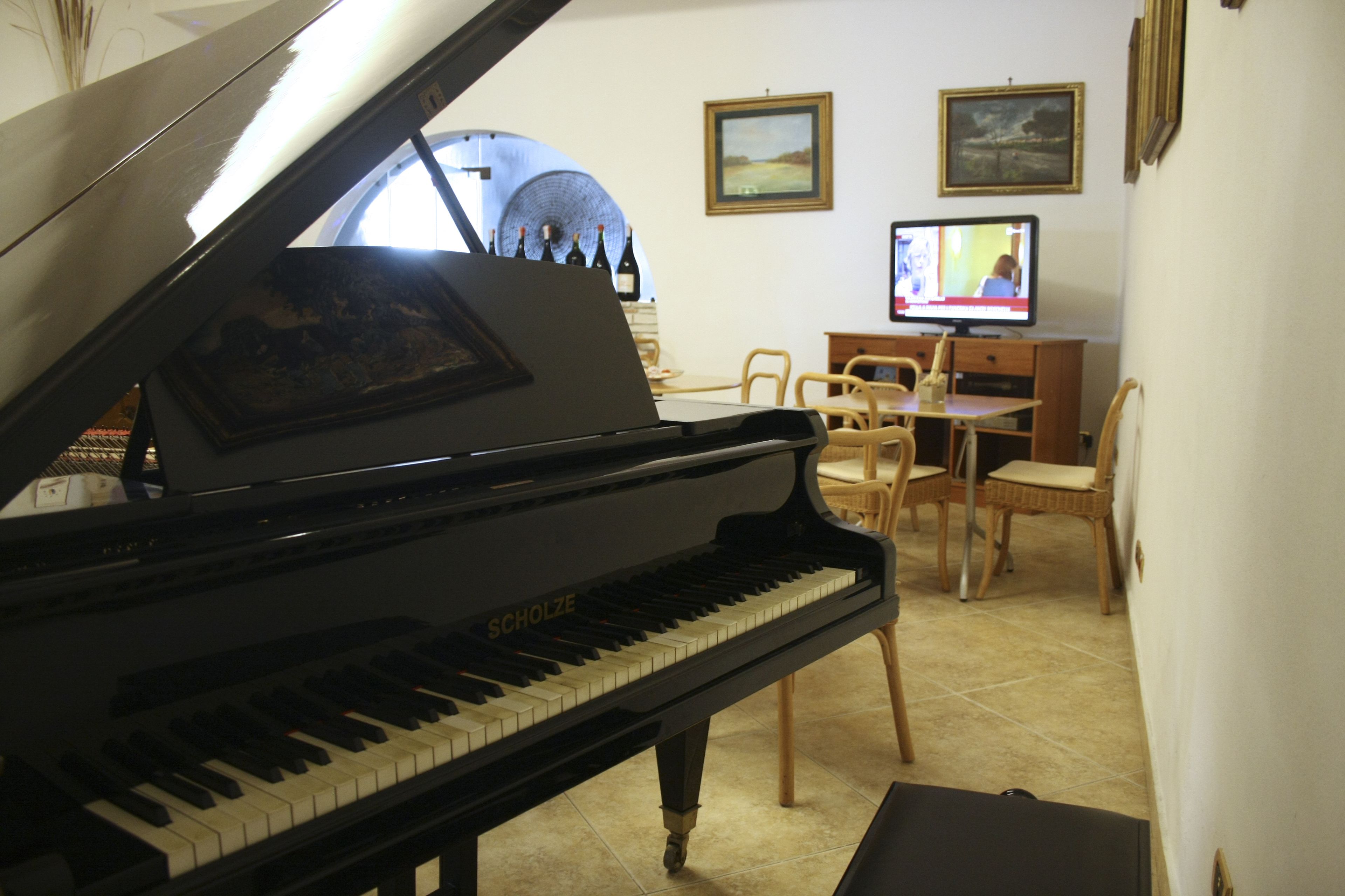 A grand piano in a room with a dining table and chairs, a television, and framed pictures on the wall.