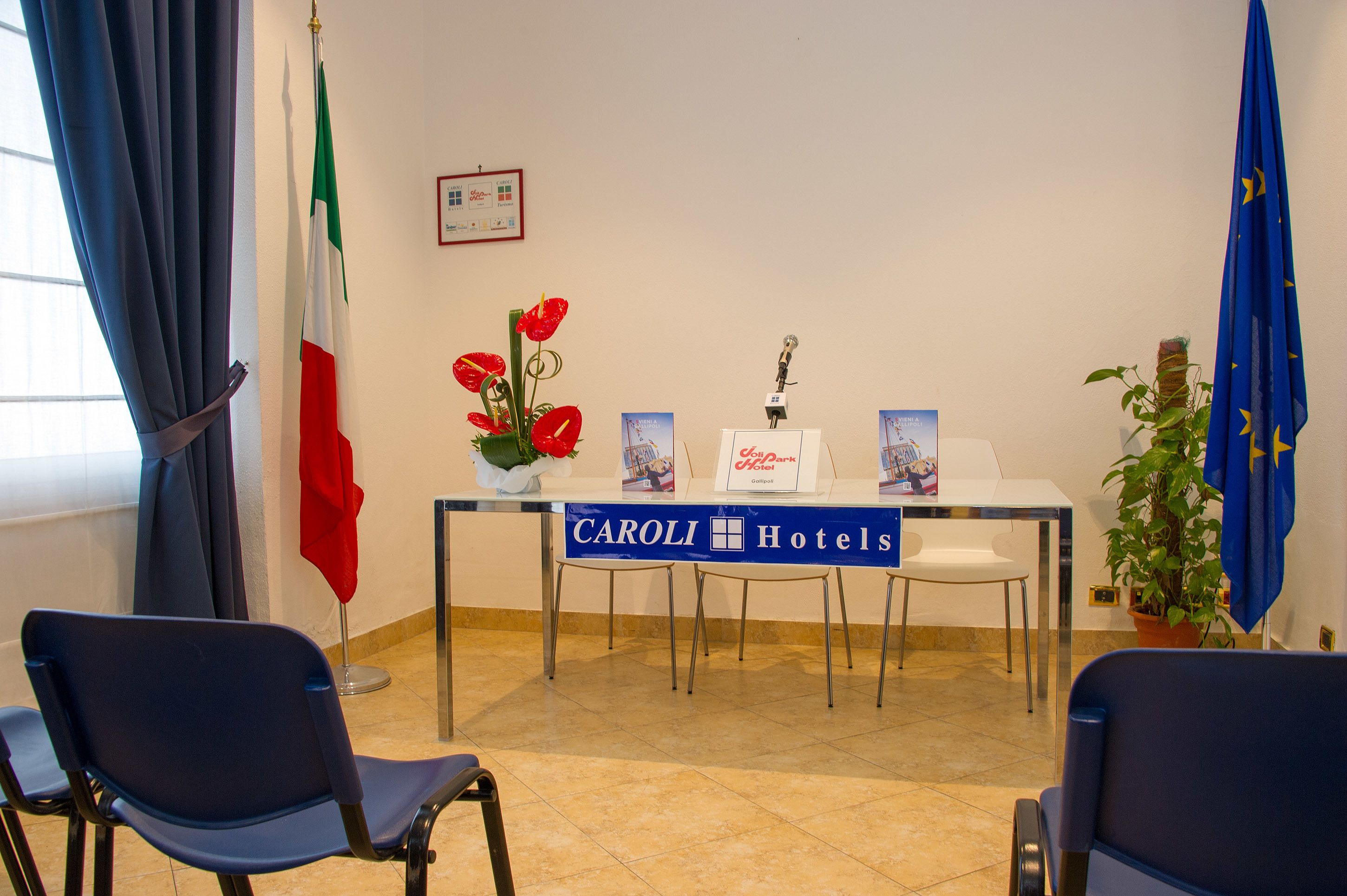 A hotel reception area with a table displaying the hotel name, flags, and a vase of red flowers.