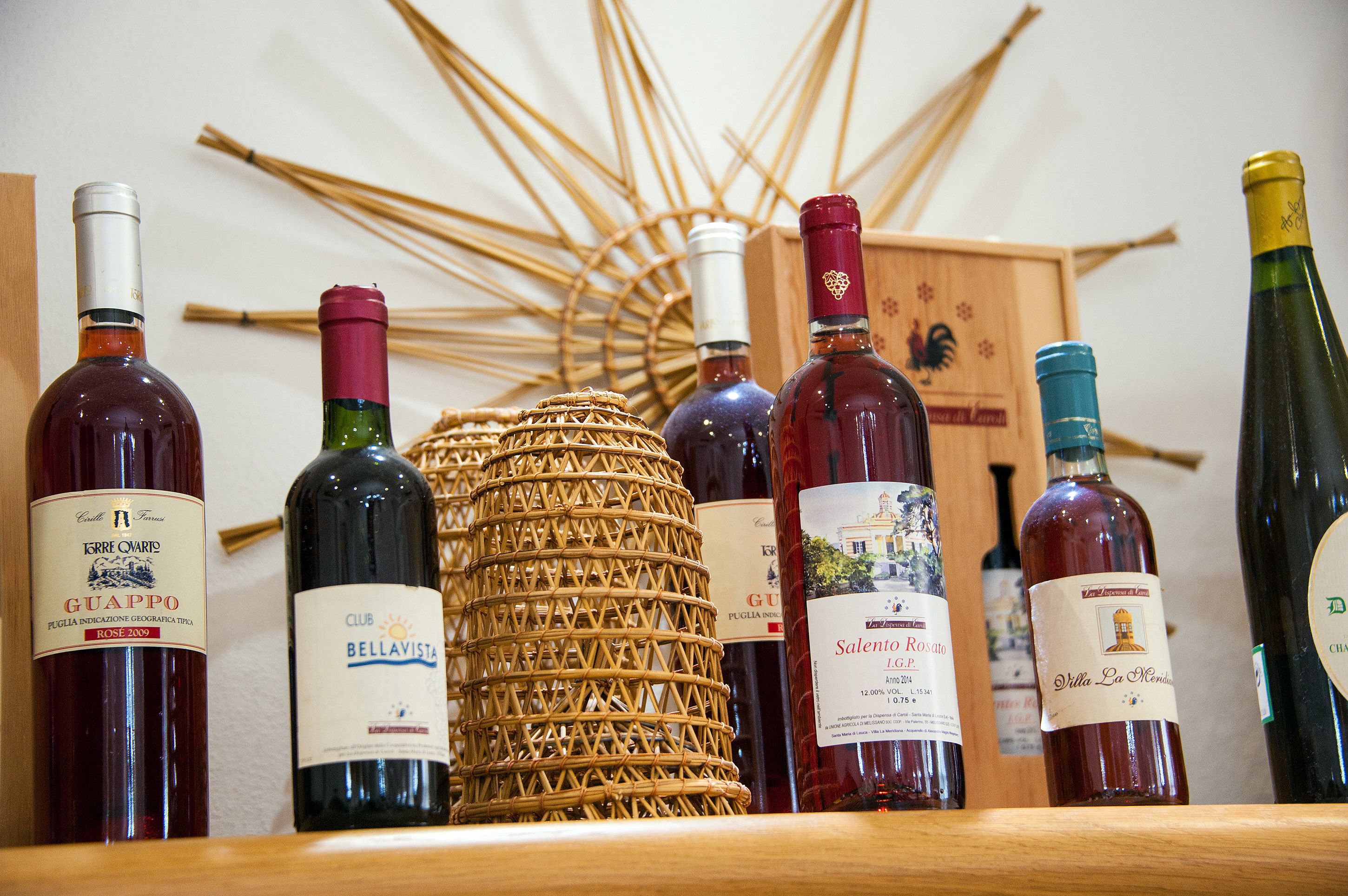 A selection of wine bottles on a shelf with a decorative woven basket in the center.