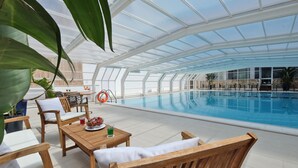 A covered outdoor swimming pool area with wooden furniture and potted plants. - Joli Park Hotel (Gallipoli)