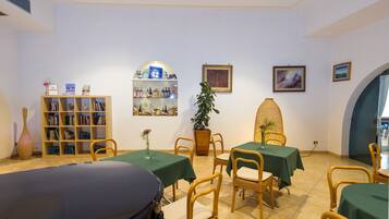 A dining area with tables and chairs, a bookshelf, and framed pictures on the walls.