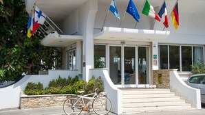 A building with a white exterior, a set of stairs leading to the entrance, and multiple flags hanging above. - Joli Park Hotel (Gallipoli)