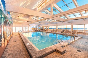 Une piscine intérieure offrant une vue dégagée sur l’océan grâce à de grandes baies vitrées.