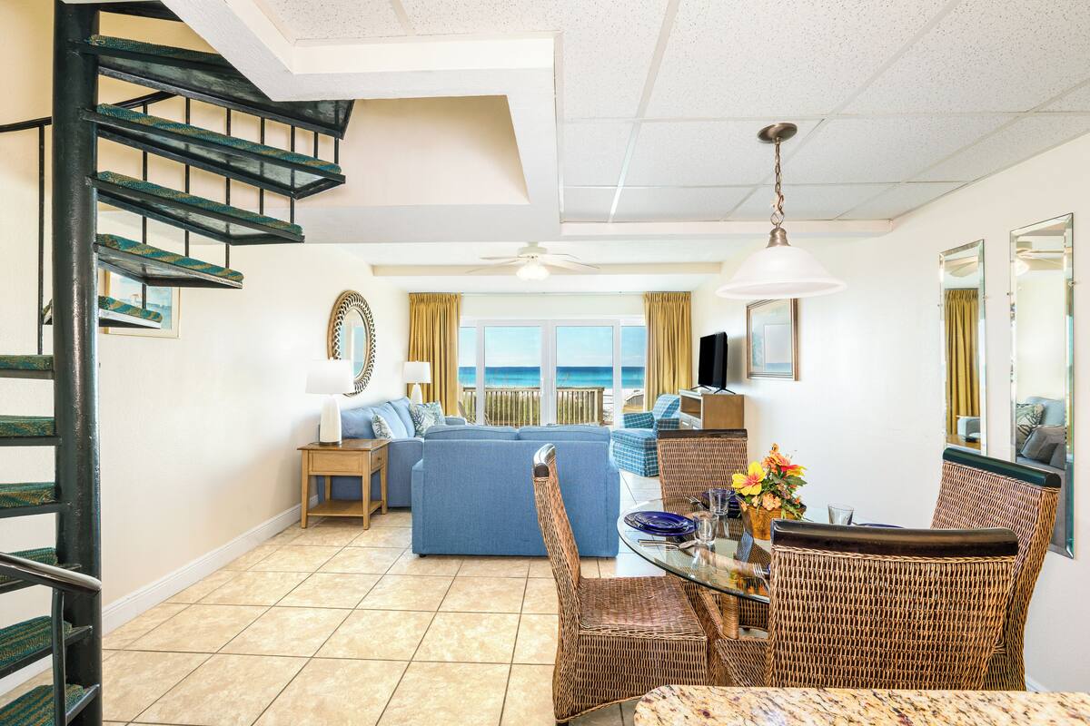 A spacious living area with a dining table, wicker chairs, a sofa, and a staircase.