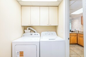 Une buanderie équipée de deux machines à laver et deux sèche-linge superposés, avec des armoires en bois au-dessus et une bouche d’aération sur le côté gauche.