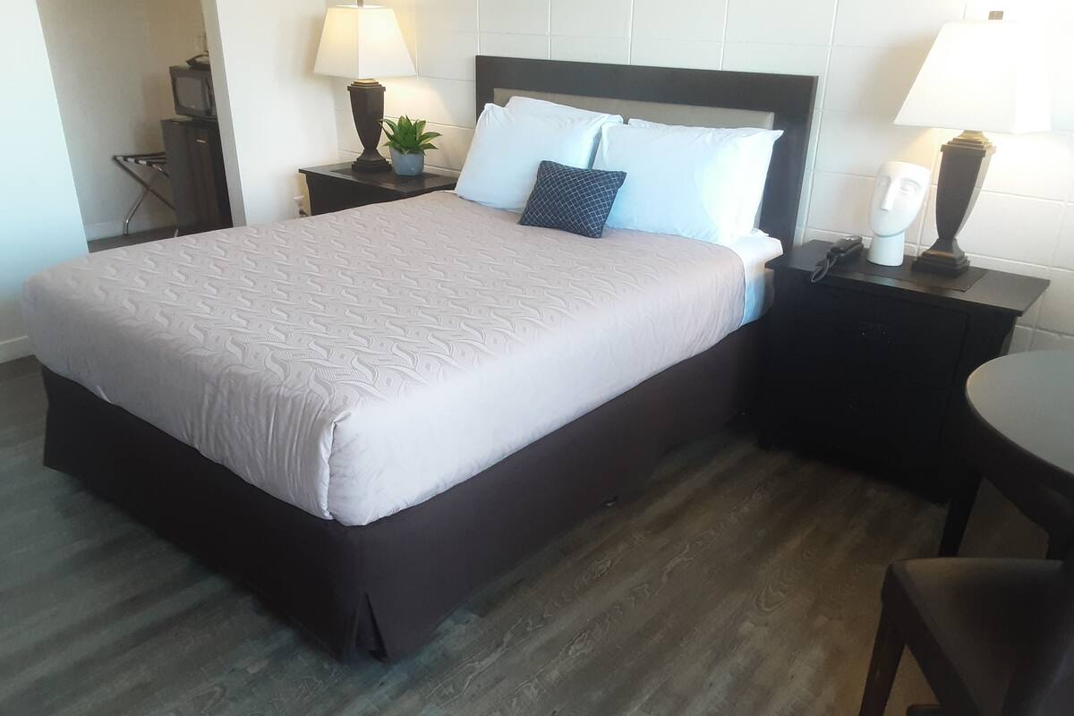 A hotel room with a large bed, two bedside tables with lamps, a small table, and a chair.