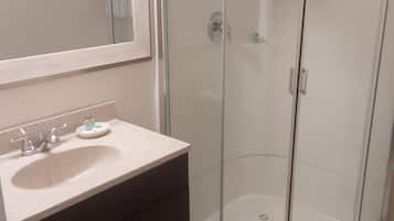 A bathroom with a glass shower enclosure, a sink with a mirror, and a dark-colored cabinet.