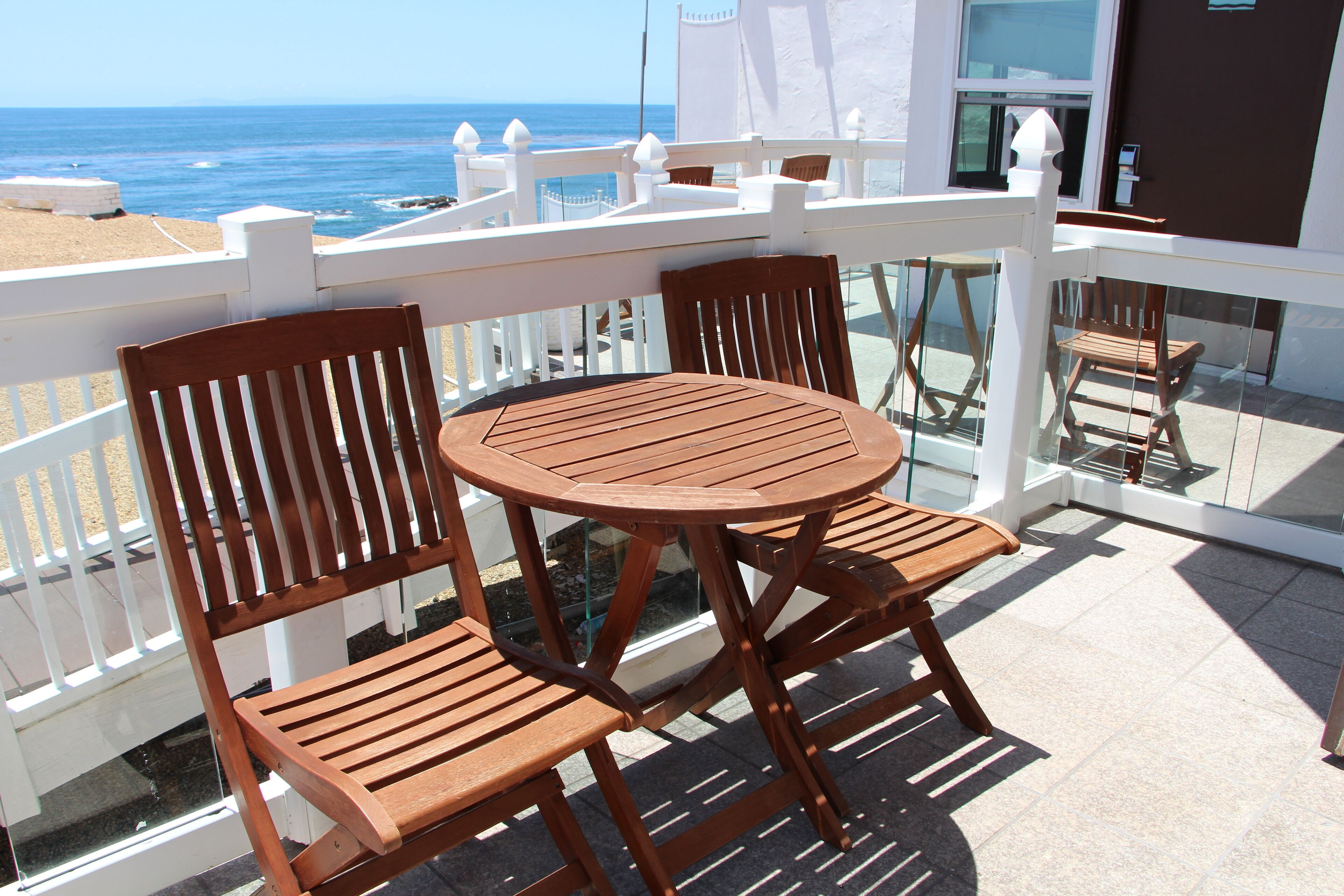 Un balcón con mesa y sillas de madera, con vista al océano.