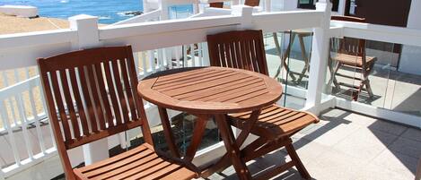 A balcony with a wooden table and chairs, overlooking the ocean.
