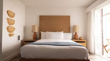 A modern bedroom with a large bed, two bedside tables with lamps, a wooden headboard, and a view of the outdoors through a sliding door.