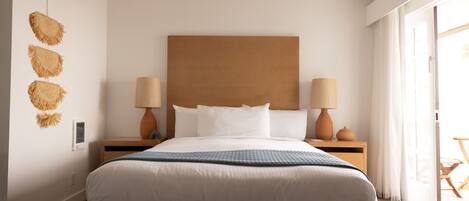 A modern bedroom with a large bed, two bedside tables with lamps, a wooden headboard, and a view of the outdoors through a sliding door.