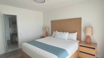 Habitación de hotel con una cama grande, cabecero de madera, dos mesitas de noche con lámparas y vistas a un baño a través de una puerta abierta.