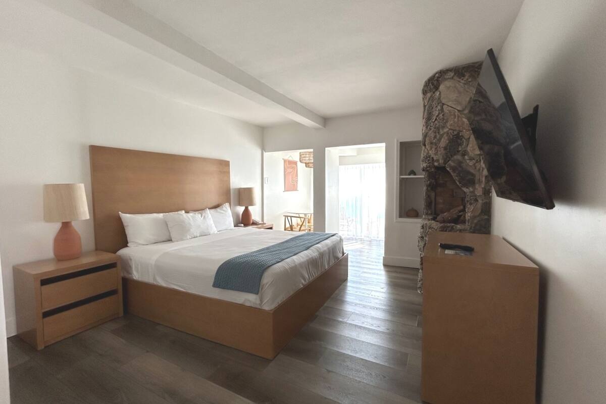 Ein modernes Hotelzimmer mit einem großen Bett, einem Holzkopfteil, Nachttischen, einem Flachbildfernseher und einer Wand mit Steinverkleidung.