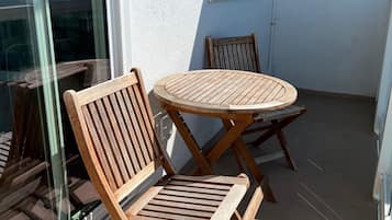 Un petit espace extérieur aménagé avec deux chaises en bois et une table ronde, situé juste à côté d’une porte vitrée.