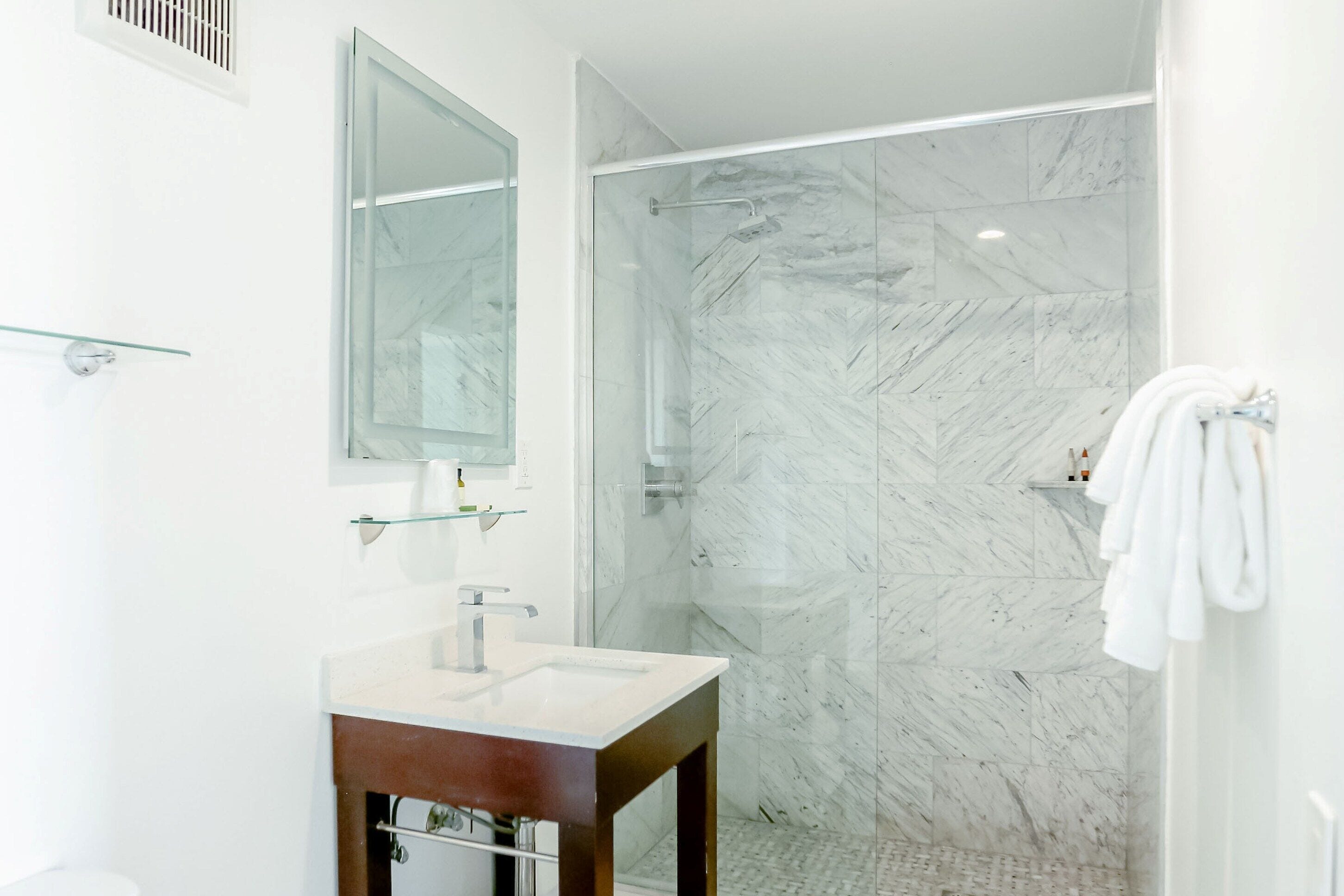 Un baño moderno con ducha de mármol, lavamanos de cristal y tocador de madera.