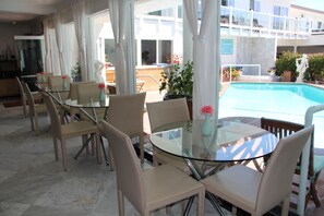 Mesa de vidrio con sillas, piscina y balcón con mobiliario exterior.