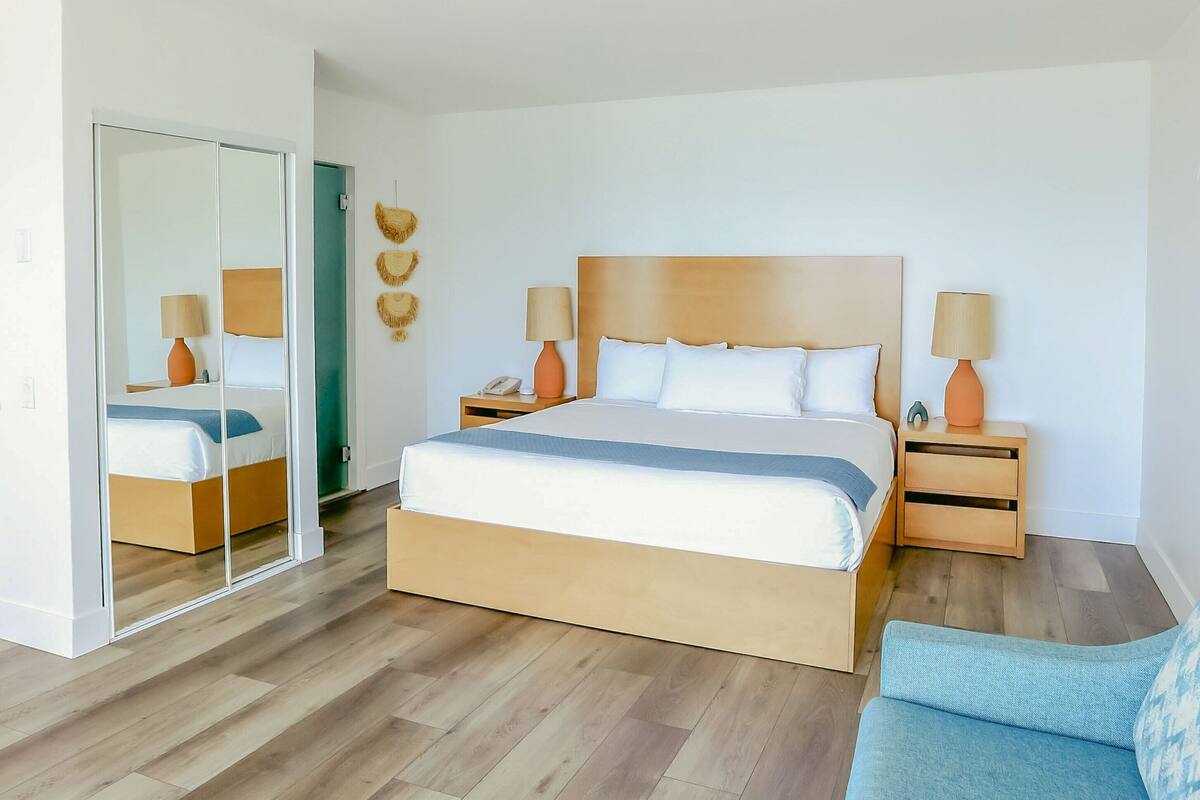 Ein modernes Hotelzimmer mit einem großen Bett, einem Holzkopfende, zwei Nachttischen mit Lampen, einem Spiegel und einem blauen Sofa.
