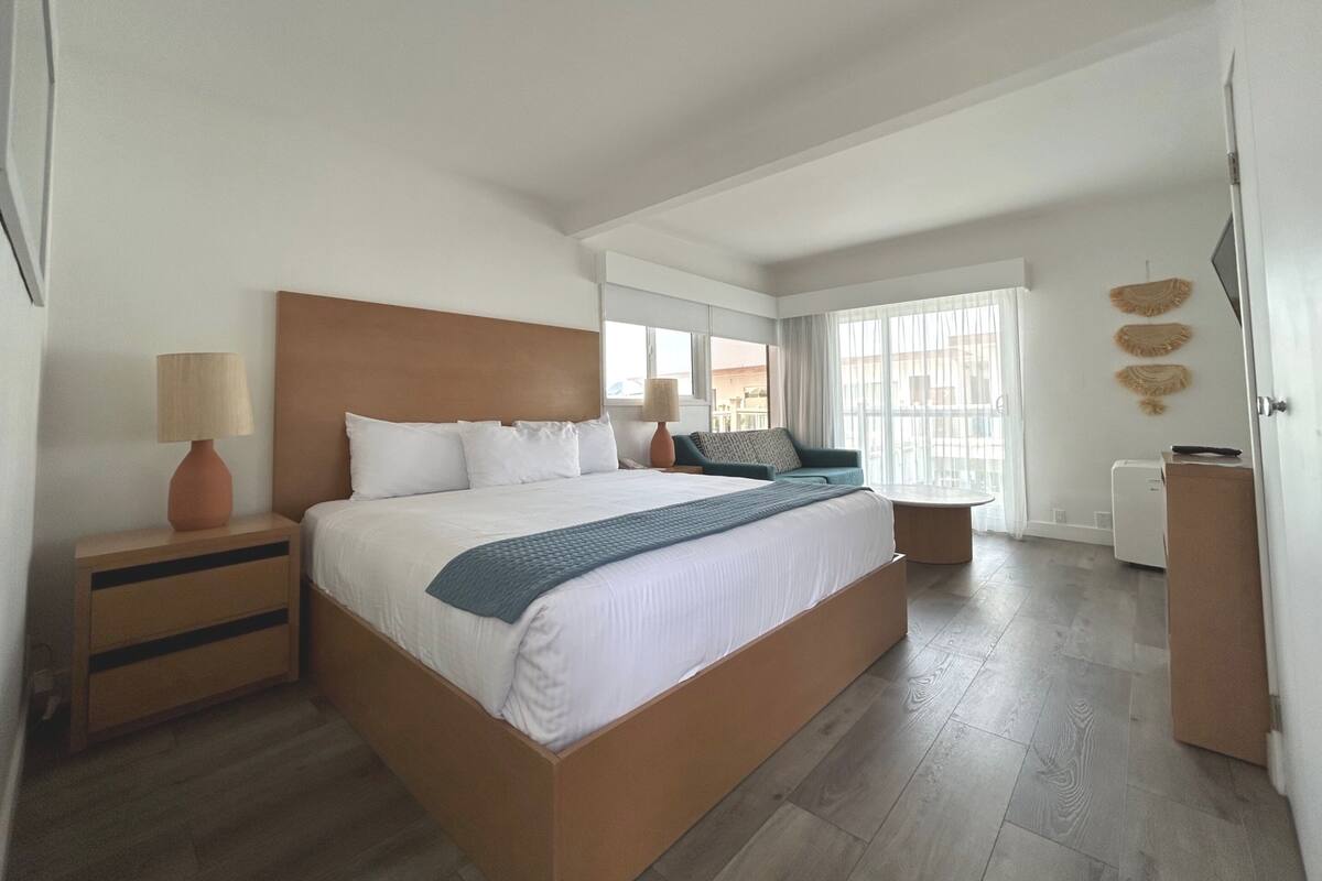 Ein modernes Hotelzimmer mit einem großen Bett, Nachttischen, einem Schreibtisch und Blick auf die Stadt.