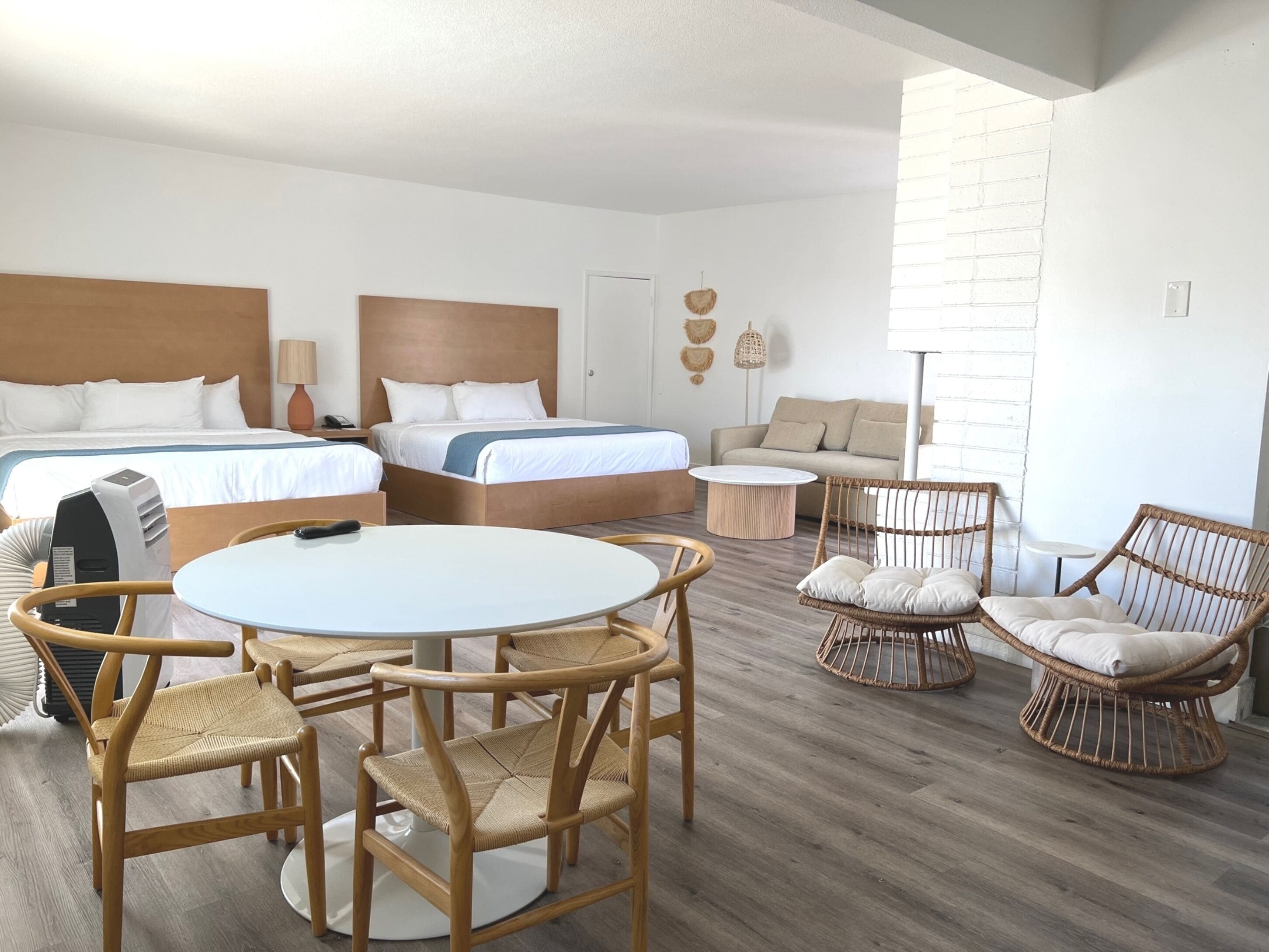 Una habitación de hotel con dos camas, una mesa de comedor redonda, sillas de mimbre, un sofá y una pequeña mesita.