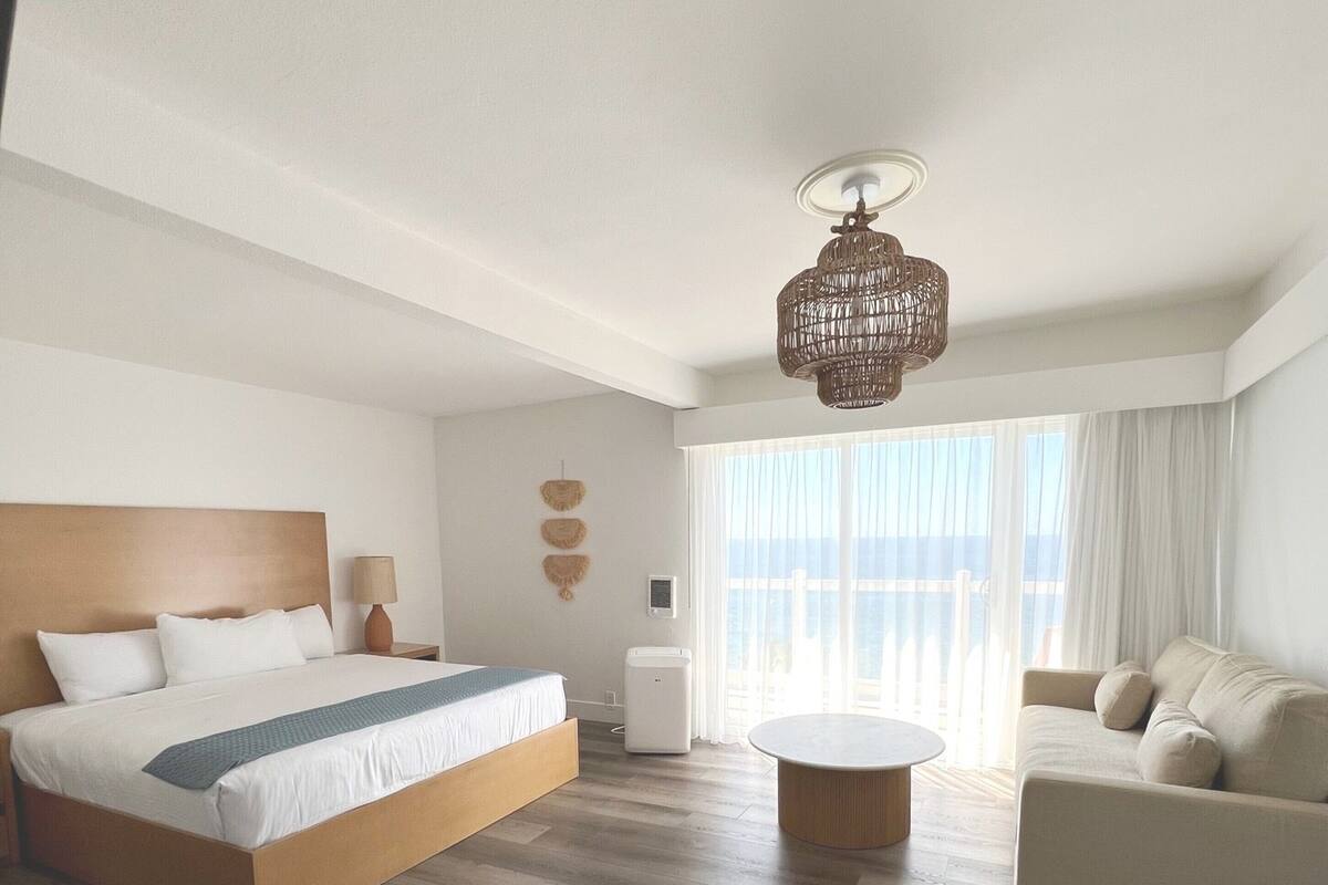 Ein modernes Hotelzimmer mit einem großen Bett, einem Sofa, einem Couchtisch und Meerblick.
