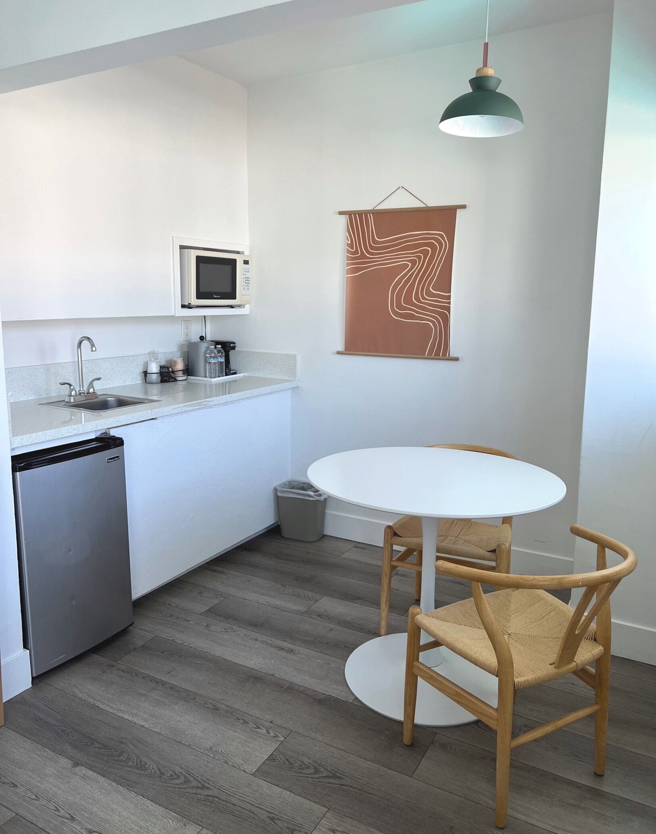 A compact kitchen with a sink, microwave, and dishwasher, a white dining table with two chairs, and a hanging pendant light.