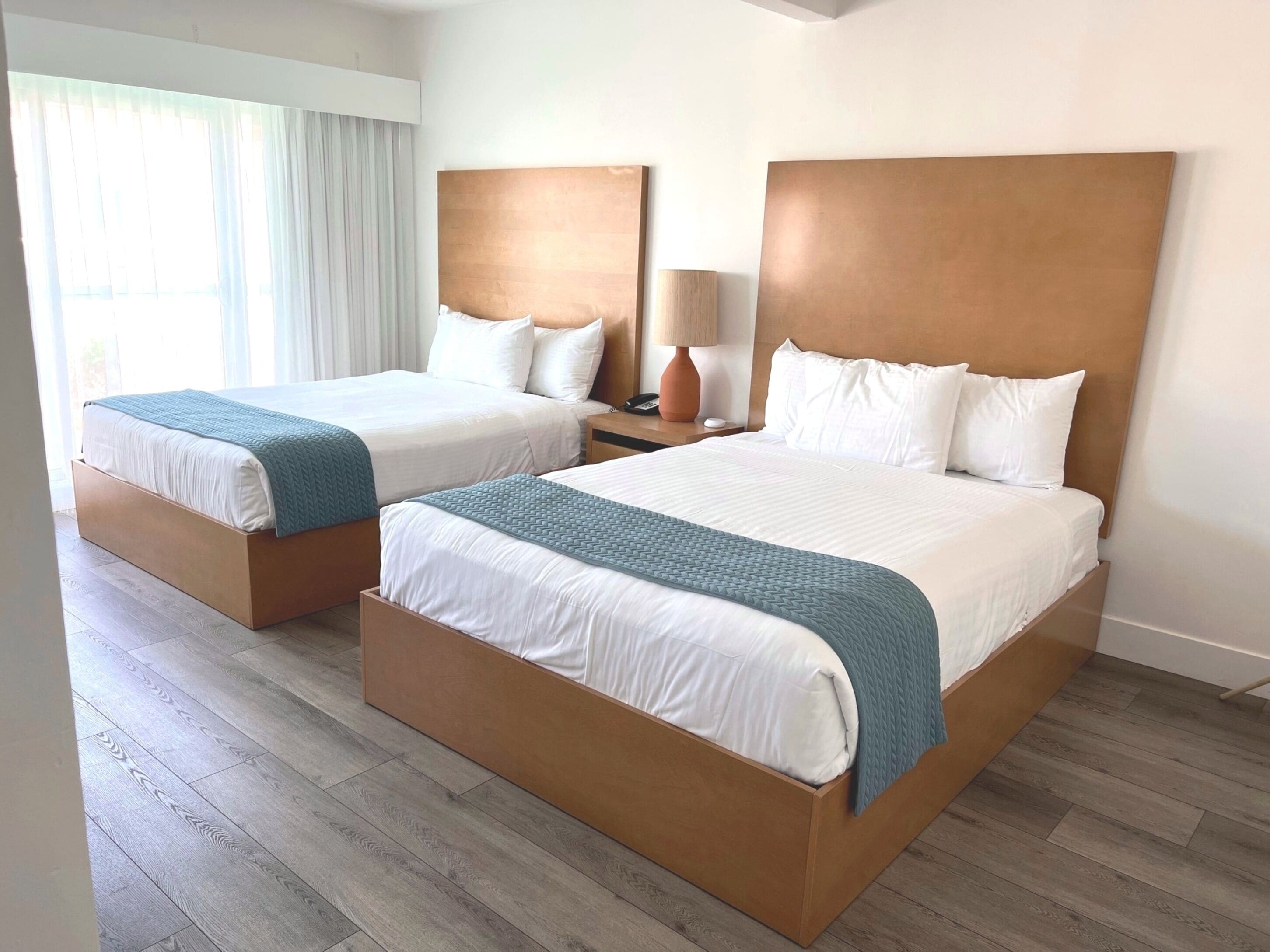 A hotel room with two beds, wooden headboards, white bedding, and a wooden floor.